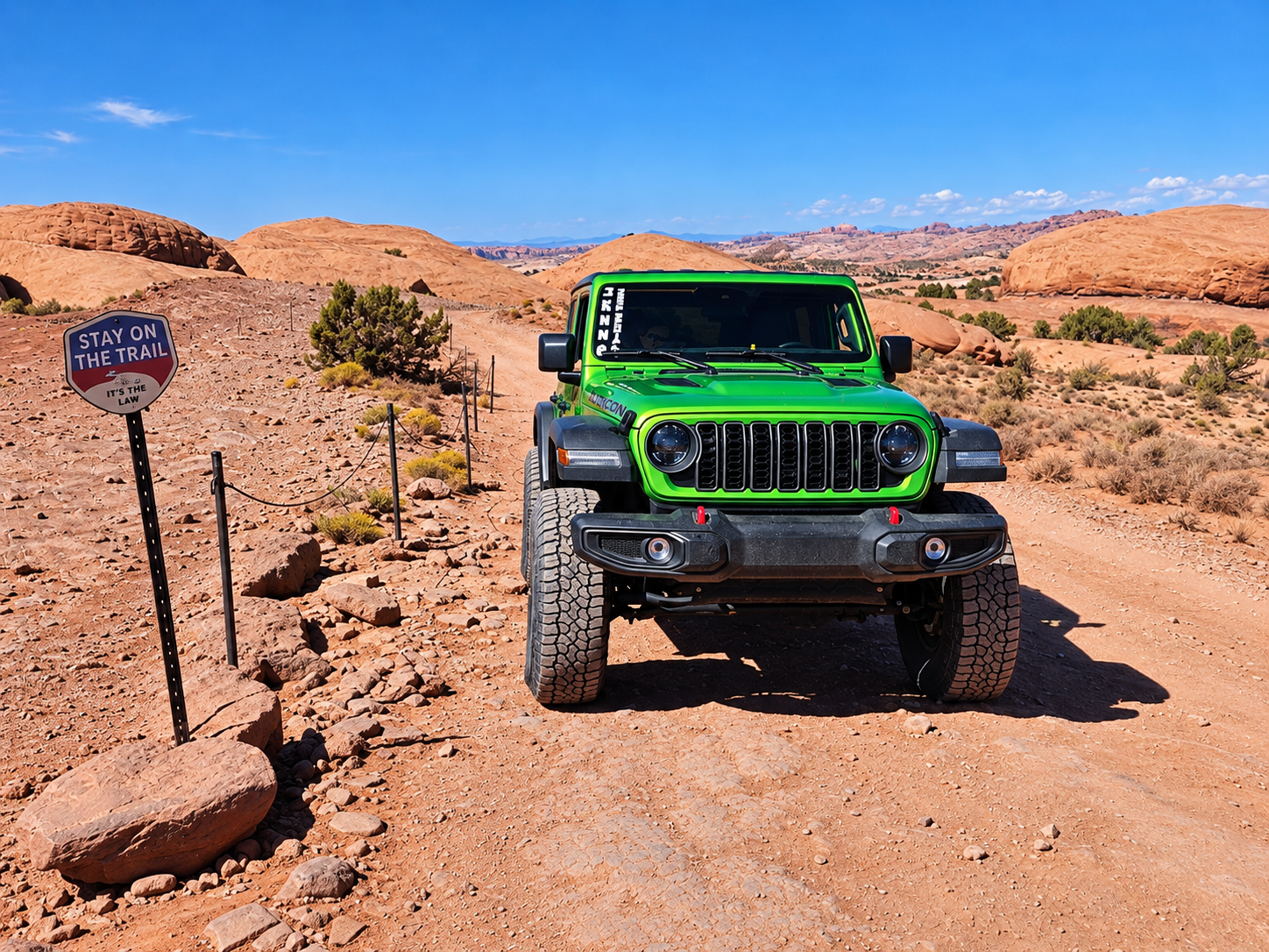 Pistachio-green Jeep Wrangler Rubicon rental on a Moab trail beside a Stay on the Trail sign
