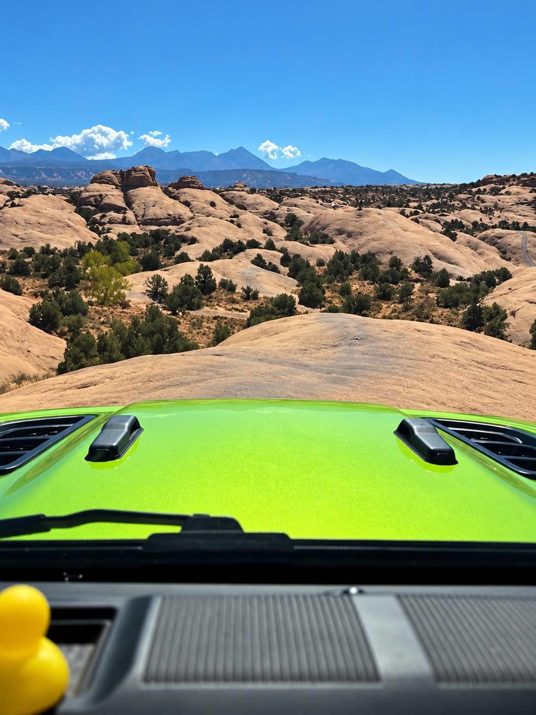 View over the hood of a green Jeep Wrangler Rubicon on Moab slickrock