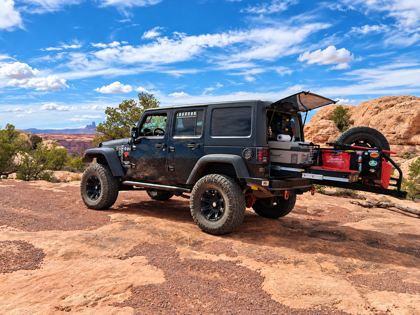 Modified black Jeep Wrangler JKU adventure rig on Moab slickrock with rear cargo system