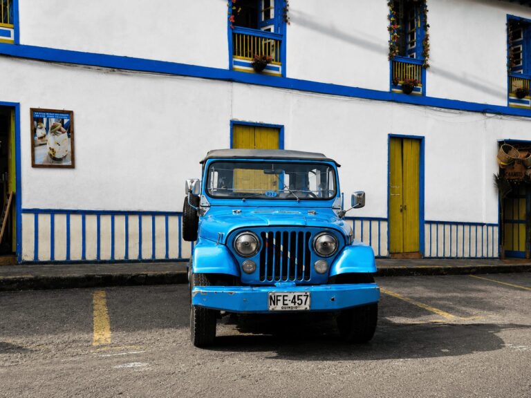 Vintage blue Willys Jeep in Colombia’s coffee region, parked in front of a white colonial building with blue trim and yellow doors, Quindío license plate