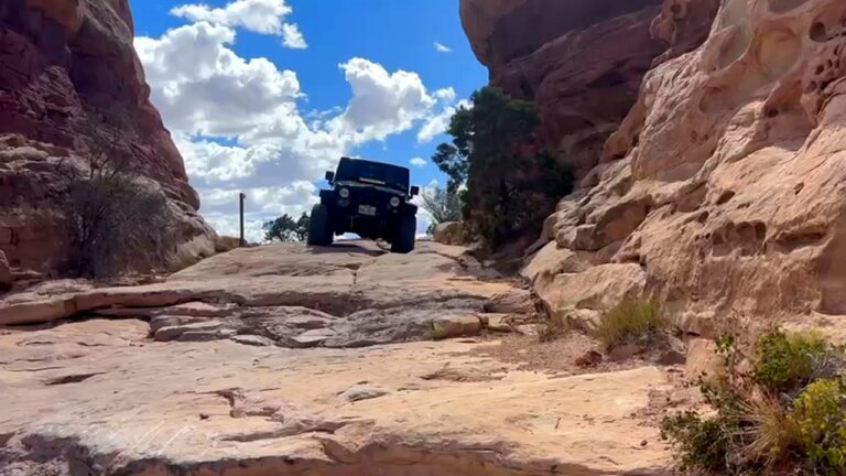 Jeep Wrangler driving over a rock ledge on the Elephant Hill trail in Canyonlands
