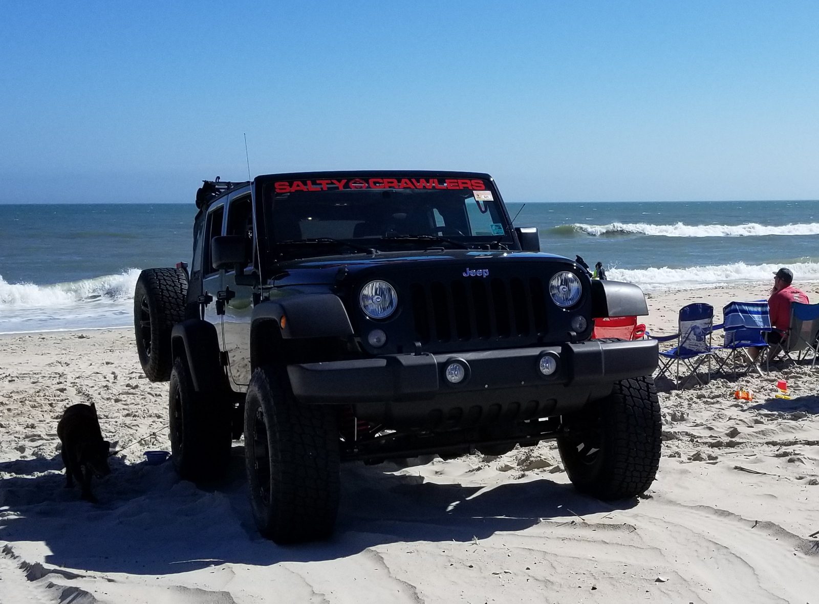Front of a lifted black Jeep Wrangler Unlimited with 35-inch tires parked on the sand at the water's edge