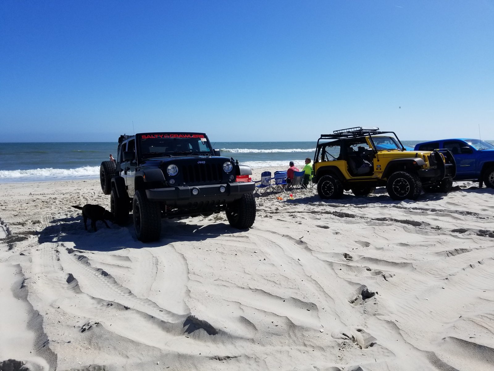 Lifted black Jeep Wrangler Unlimited on a beach next to a yellow Jeep and a blue truck