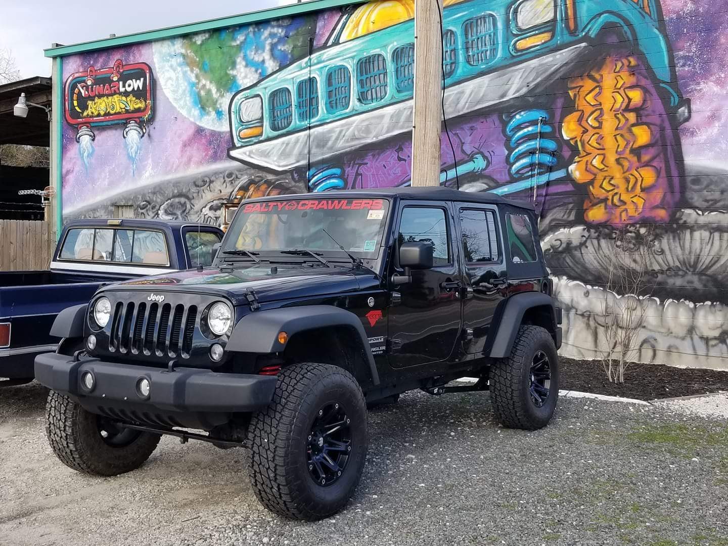 Black Jeep Wrangler Unlimited with a 4-inch long arm lift, new wheels, and 35-inch tires parked in front of a mural