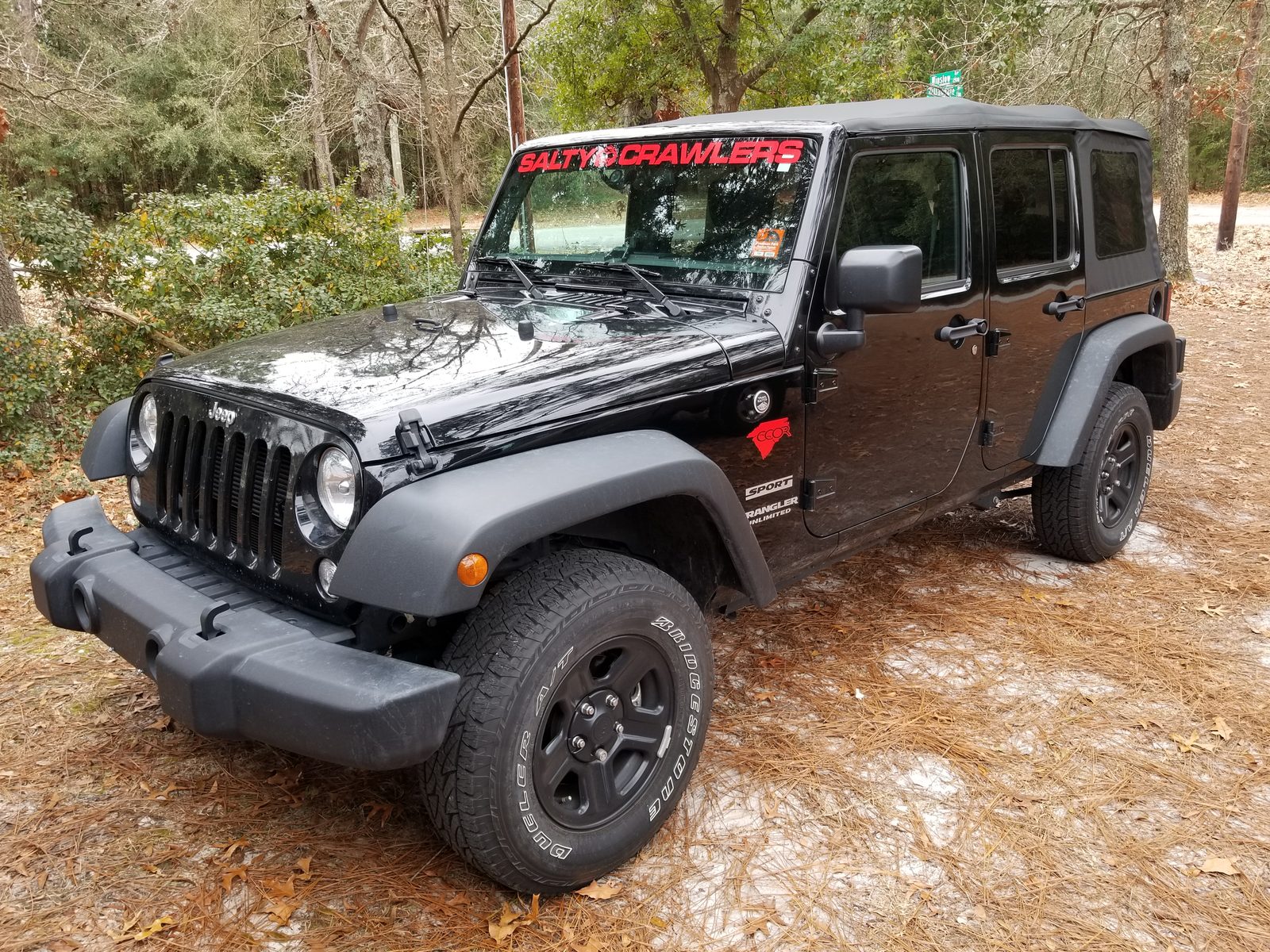 Front three-quarter view of a stock Jeep Wrangler Unlimited with factory wheels and Bridgestone Dueler A/T tires