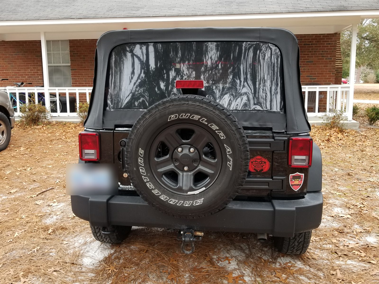 Rear of a stock Jeep Wrangler Unlimited showing the soft top and factory spare tire
